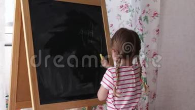 学龄前小女孩在黑板上写字母。 幼儿女孩拿着粉笔画画。